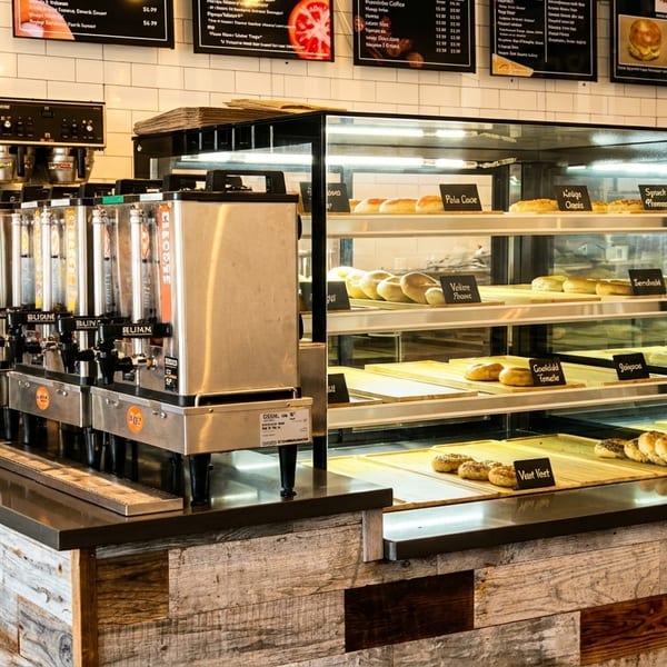 Rustic cafe counter with coffee dispensers and a glass case of fresh baked goods.