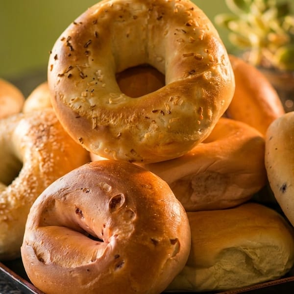 Assortment of freshly baked bagels, including sesame, onion, and blueberry, on a dark tray.